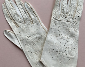 Könnte beinhalten: Ein Paar weiße Lederhandschuhe mit einem zarten, gemusterten Design. Die Handschuhe haben einen dezenten Glanz und sind aus weichem, geschmeidigem Leder gefertigt.