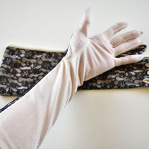 May include: Elegant, long, cream-colored gloves with black lace detailing. The gloves are made of a soft, velvety material and feature a delicate floral lace pattern on the back of the hand and along the arm. A classic accessory for formal events.