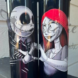 Puede incluir: Dos vasos de acero inoxidable negros con Jack Skellington y Sally de The Nightmare Before Christmas. Los vasos tienen un borde negro con cuentas y el texto "Tumblers stainless/ Vasos T&eacute;rmicos" en la parte inferior.