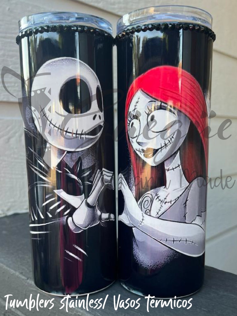 Puede incluir: Dos vasos de acero inoxidable negros con Jack Skellington y Sally de The Nightmare Before Christmas. Los vasos tienen un borde negro con cuentas y el texto "Tumblers stainless/ Vasos T&eacute;rmicos" en la parte inferior.