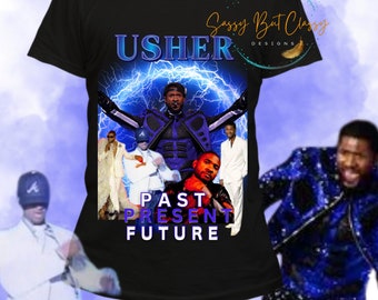 May include: Black t-shirt with a graphic of Usher in a blue and white outfit with the text "USHER" in white and "PAST PRESENT FUTURE" in purple. The background is a blue and white lightning bolt design.