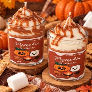 Peut inclure: Deux bougies en verre surmontées de tourbillons de cire blanche et d'un filet couleur caramel. Les étiquettes portent l'inscription "Pumpkin S'more" et "Megans Gift Haven" avec des illustrations de citrouille, guimauve et feu de camp.