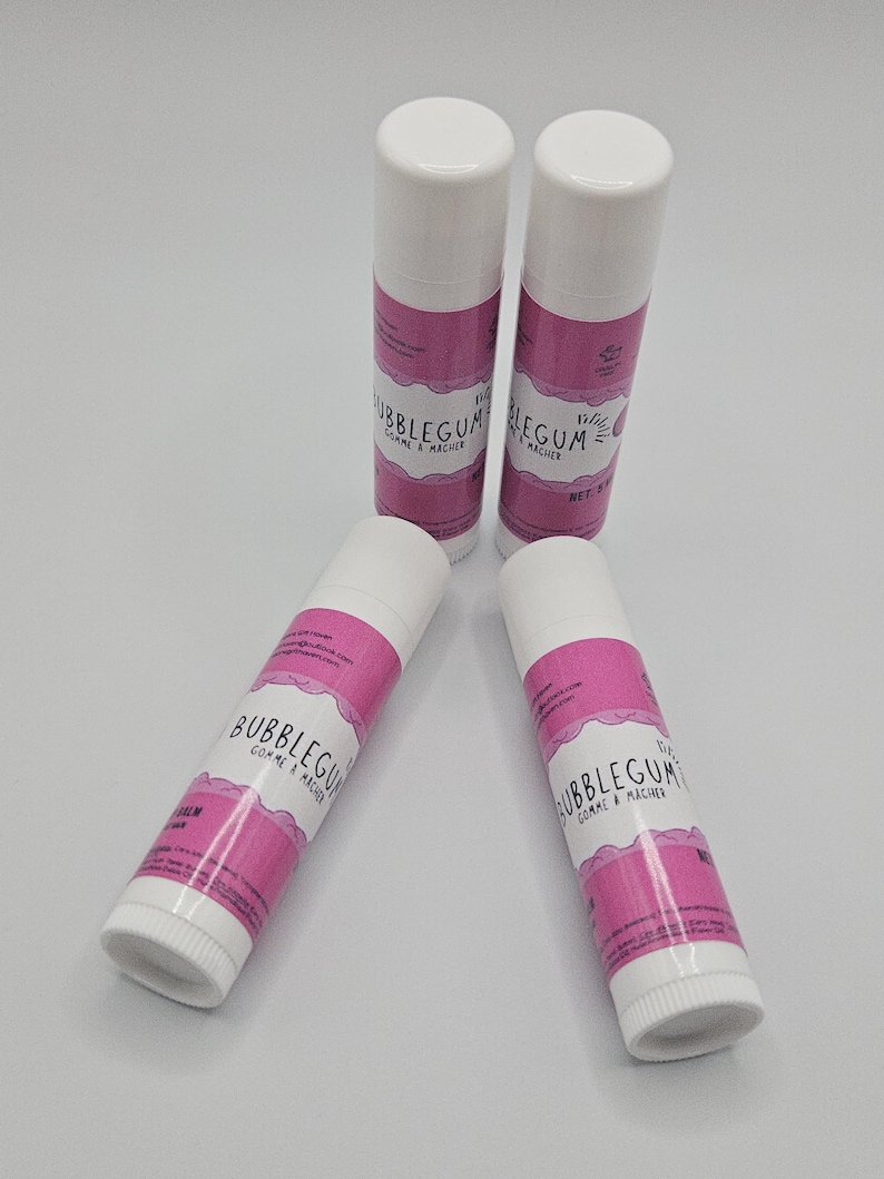 May include: Four white lip balm tubes with pink labels. The labels read "Bubblegum Comme & Macher". The tubes are arranged in a circular pattern against a white background. The lip balms are a cosmetic product.