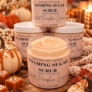 Peut inclure: Quatre pots ronds en plastique de gommage sucré moussant Megans Gift Haven au parfum White Pumpkin Caramel. Chaque pot possède un couvercle blanc et une étiquette rose pâle avec du texte noir indiquant le nom et un poids net de 283 grammes.