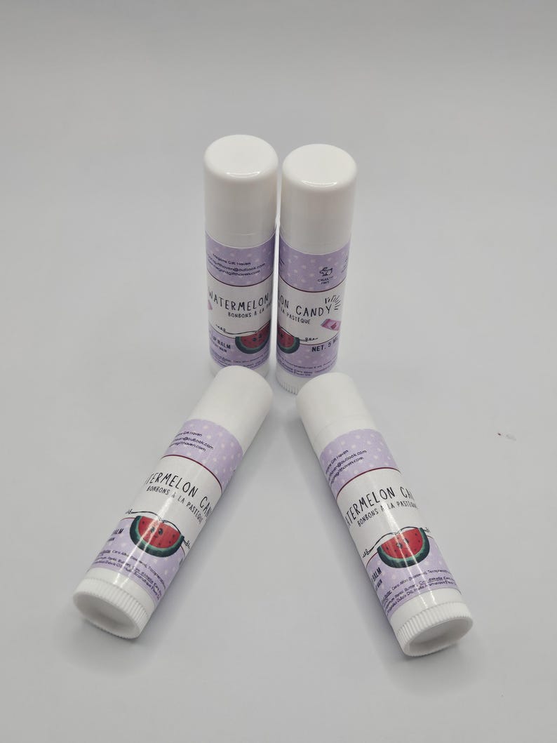 May include: Four white lip balm tubes with white caps are arranged on a white surface. Each tube has a purple label with the words "Watermelon Candy" and a watermelon slice graphic. The net weight is 0.15 oz.