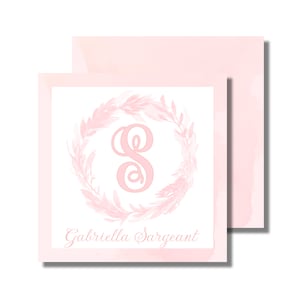 May include: A pink watercolor background with a white square overlay. The square features a pink floral wreath with a pink letter "S" in the center. The text "Gabriella Sargeant" is written in cursive below the wreath.