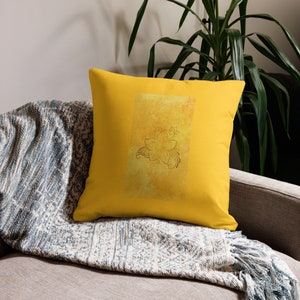 May include: A yellow throw pillow with a floral design in a lighter shade of yellow. The pillow is on a couch with a blue and white throw blanket.