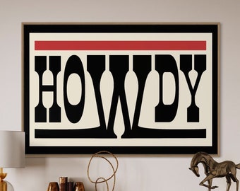 May include: A framed art print with the word "HOWDY" in bold black letters on a cream background, with a red stripe at the top. The artwork hangs above a wooden cabinet with decorative items, including a bronze horse statue and a gold lamp.