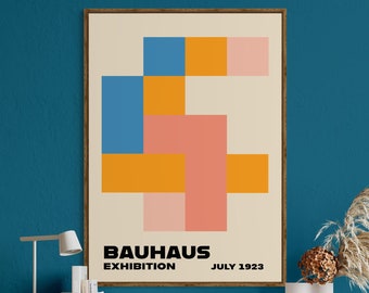 May include: A framed poster with a geometric design in shades of blue, orange, and pink. The poster reads "Bauhaus Exhibition July 1923". The poster is hanging on a teal wall above a wooden desk with a brown leather office chair.