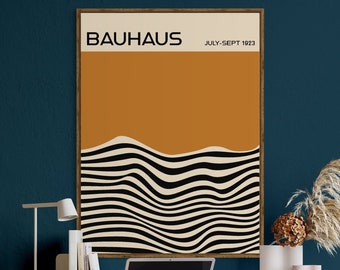 May include: A framed poster with the text "BAHAUS JULY-SEPT 1923" and a black and white abstract design on a brown background. The poster is hanging on a teal wall above a wooden desk with a brown leather office chair, a laptop, and a lamp.