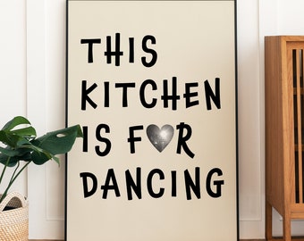 May include: A black framed poster with a beige background and the text "This Kitchen is for Dancing" with a silver glitter heart in the middle of the text.