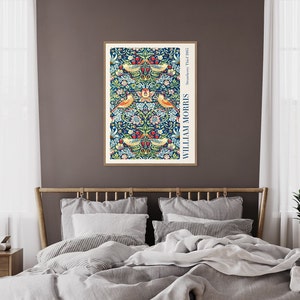 Puede incluir: Una impresi&oacute;n enmarcada de un patr&oacute;n floral vintage con p&aacute;jaros y el texto "Strawberry Thief 1883" y "WILLIAM MORRIS" en un marco blanco sobre una pared marr&oacute;n encima de una cama con ropa de cama gris.