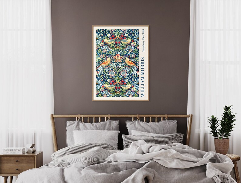 Puede incluir: Una impresi&oacute;n enmarcada de un patr&oacute;n floral vintage con p&aacute;jaros y el texto "Strawberry Thief 1883" y "WILLIAM MORRIS" en un marco blanco sobre una pared marr&oacute;n encima de una cama con ropa de cama gris.