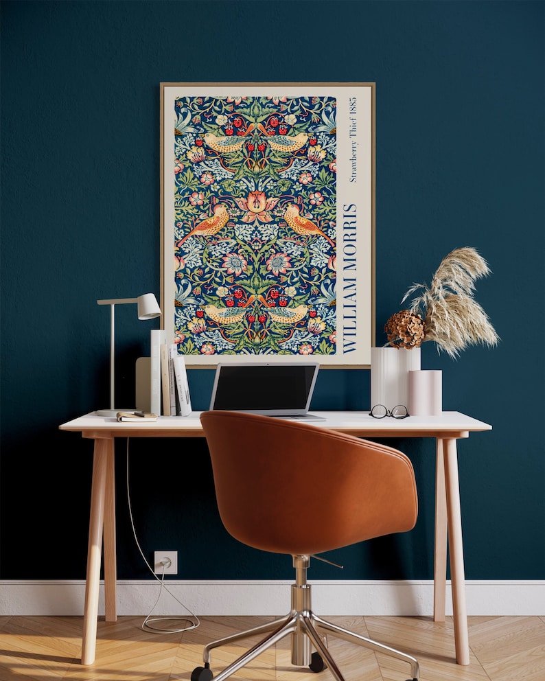 Puede incluir: Un escritorio de oficina en casa con una tapa y patas de madera marr&oacute;n claro. Un ordenador port&aacute;til, una l&aacute;mpara y una impresi&oacute;n enmarcada de un patr&oacute;n floral con p&aacute;jaros est&aacute;n en el escritorio. Una silla de oficina de cuero marr&oacute;n est&aacute; delante del escritorio. La pared detr&aacute;s del escritorio es de color azul turquesa oscuro.