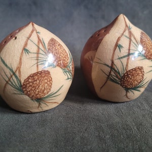 以下が含まれることがあります： 茶色と白の釉薬をかけたセラミック製の塩とコショウ入れ2つ。塩入れは松ぼっくり型で、松葉と松ぼっくりのデザインが施されています。