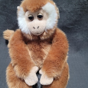 May include: A plush monkey toy with brown fur and a white face and ear accents. The stuffed animal has a small tail and is sitting upright. The monkey's eyes are dark and it has a neutral expression. The toy is made of soft, fuzzy material.