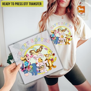 May include: A white t-shirt with a colorful graphic of Winnie the Pooh and friends dressed in Easter costumes. The graphic says "Happy Easter" in a rainbow font.