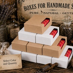 May include: A stack of rectangular cardboard soap boxes in white and kraft brown colors, each featuring a rectangular cutout window that reveals a bar of soap with a pink and orange swirl pattern. A small sign reads Select Color and Quantity.