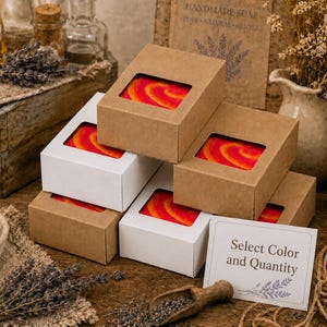 May include: A stack of rectangular soap boxes with clear windows, revealing bars with a vibrant red and orange swirl pattern. The boxes are made of brown kraft paper and white cardstock. A small white card with the text Select Color and Quantity.