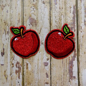 May include: Two red glitter apple iron-on patches with green leaves and stems.