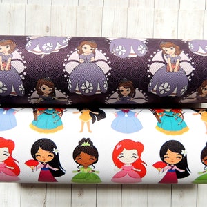 Peut inclure: Deux rouleaux de tissu sur le thème des princesses. Le rouleau du haut a un fond violet foncé avec un motif répété d'une princesse dans une robe violette avec des fleurs blanches. Le rouleau du bas a un fond blanc avec un motif répété de différentes princesses dans diverses robes.