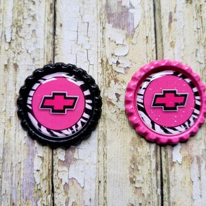 May include: Two round bottle caps with a pink and black zebra print design. The centre of each cap features a pink Chevrolet logo.