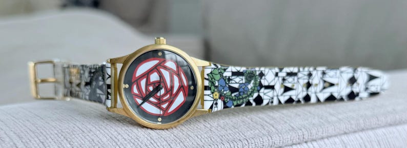 May include: A gold wristwatch with a white and black patterned band. The watch face features a red and white rose design.