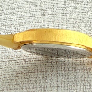 May include: A gold-tone wristwatch with a silver face. The watch has a brushed metal band.