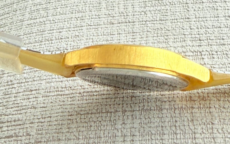 May include: A gold-tone wristwatch with a silver face. The watch has a brushed metal band.