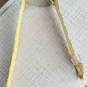 May include: A gold-toned wristwatch with a square face and a yellow patterned band. The watch is lying on a textured surface.