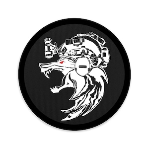 May include: A round, black patch featuring a white illustration of a wolf's head wearing tactical gear. The wolf has a red eye and the design includes intricate details of the gear.