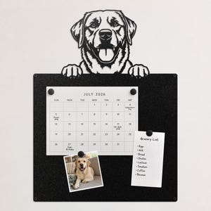 May include: A black metal magnetic board featuring a cutout of a dog head with paws resting on the top edge. The board holds a July 2026 calendar, a grocery list, and a photograph of a yellow Labrador, all secured with small black magnets.