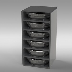 May include: A gray, vertical storage unit with five compartments, each holding a circular, metallic object. The unit has a rounded top and a smooth, modern design. The objects appear to be containers or components.