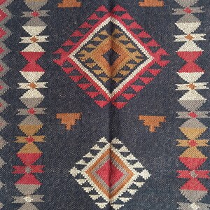 May include: A dark blue woven rug with geometric patterns. The rug features diamond and triangle shapes in red, orange, white, and tan. The design is symmetrical, with repeating patterns along the edges.