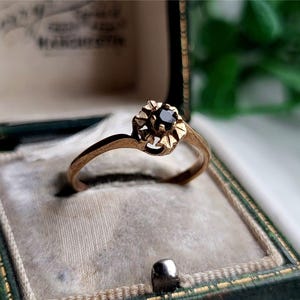 以下が含まれることがあります： 星型のデザインに黒い宝石がセットされた金の指輪。指輪は緑色のベルベット製の指輪箱に入っています。