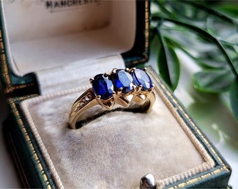 May include: A gold ring featuring three oval-shaped blue sapphires and small diamonds set in the band.