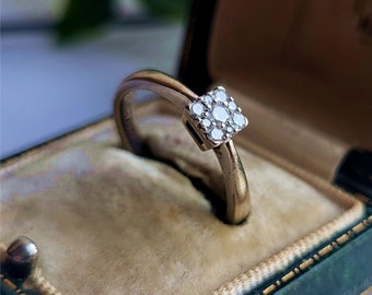 Puede incluir: Un delicado anillo de oro con un engaste cuadrado que presenta un grupo de pequeños diamantes.