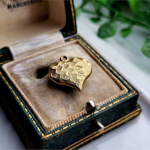 May include: A gold heart-shaped pendant with a woven pattern, displayed in a green velvet jewellery box.