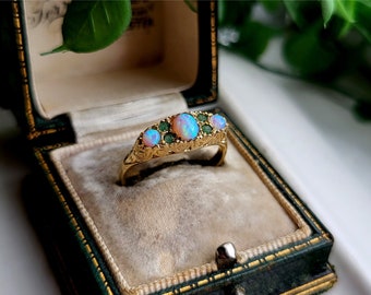 May include: A gold ring with three opal gemstones and green accents. The ring is in a green velvet ring box.