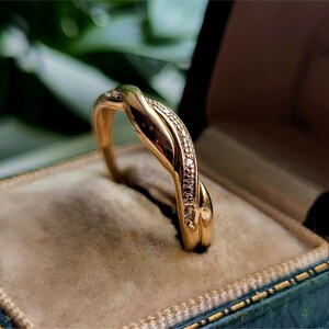 K&ouml;nnte beinhalten: Ein goldener Ring mit einem gedrehten Design und kleinen Diamanten, die in die Band eingefasst sind.
