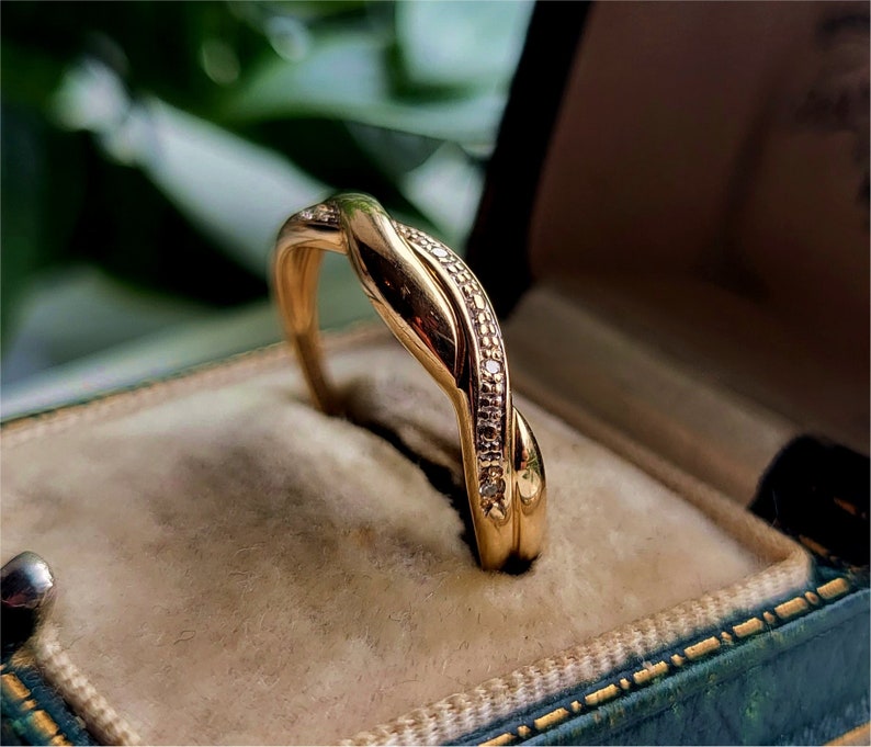 K&ouml;nnte beinhalten: Ein goldener Ring mit einem gedrehten Design und kleinen Diamanten, die in die Band eingefasst sind.
