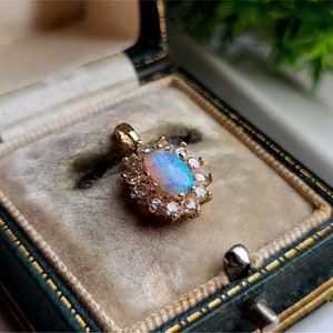 May include: A gold pendant featuring a white opal gemstone surrounded by a halo of smaller clear gemstones.