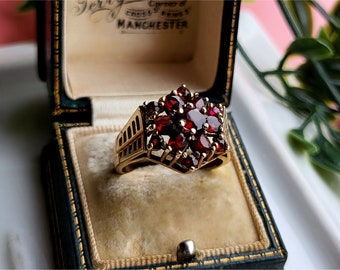 May include: A gold ring with a large red gemstone cluster in the center. The ring is in a velvet-lined box with the inscription "Corner of Cross Street, Manchester".