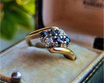 May include: A gold ring featuring a cluster of blue sapphires and white diamonds. The ring is set in a twisted band.