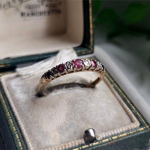 May include: A gold band ring with alternating red rubies and white diamonds. The ring is in a green velvet ring box.