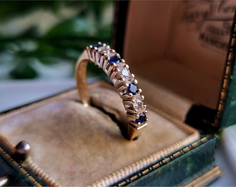 May include: A gold band ring with alternating blue sapphires and white diamonds. The ring is in a green velvet ring box.