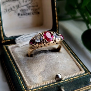May include: A gold ring with a large red ruby and smaller white diamonds set in a filigree design. The ring is in a green velvet ring box.