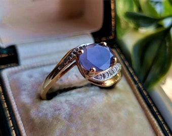 May include: A gold ring with a large oval purple gemstone surrounded by smaller diamonds. The ring is set in a white gold band.