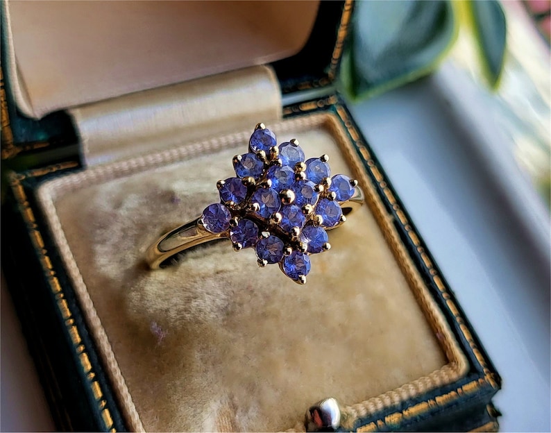 May include: A gold ring with a cluster of purple gemstones set in a flower shape.