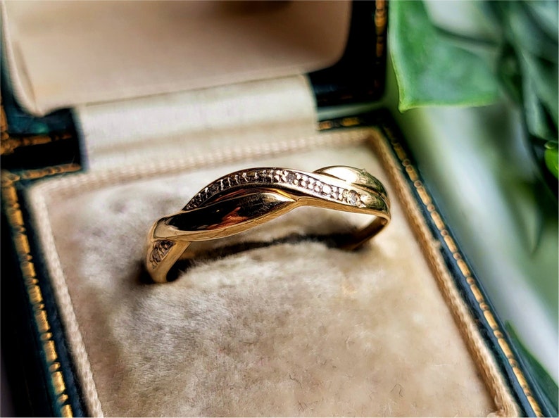 K&ouml;nnte beinhalten: Ein Goldring mit einem gedrehten Design und kleinen Diamanten, die in die Band eingefasst sind.